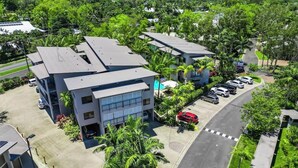 A modern building with a flat roof, multiple parking spaces, and surrounding greenery. - Laguna Escape—Swim-Out Retreat near Sea & Dining (Trinity Beach)