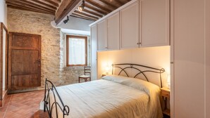 Ein Schlafzimmer mit Bett, Holzschrank, Steinwand und Fenster.