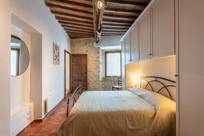 Un dormitorio con cama, vigas de madera, pared de piedra y una ventana.