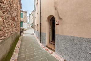 Un callejón estrecho con un camino de piedra, un edificio con el número '1' y una pared de piedra en un lado.