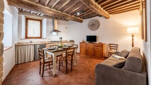 Eine rustikale Küche mit Holzbalken, einem Esstisch mit Stühlen, einer Couch und einem Fernseher.