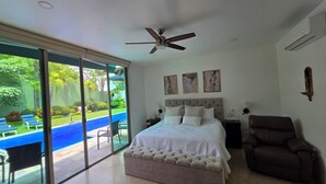 Quarto com cama, cadeira, ventilador de teto e vista para uma piscina.