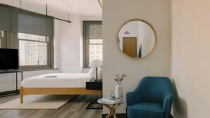 Een moderne hotelkamer met een bed, een ronde spiegel, een blauwe fauteuil en een tafeltje met een vaas.