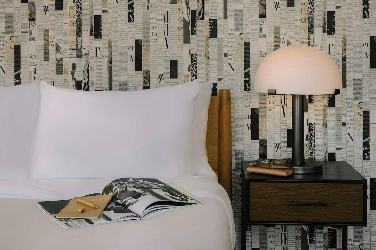 A neatly made bed with a magazine, a lamp, and a nightstand with a drawer.