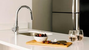 Een moderne keuken met een wit aanrecht, roestvrijstalen apparatuur, een zwarte hanglamp en een schaal kersen.