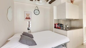 A bedroom with a bed, pillows, a bedside table, a wall clock, and a framed picture. - Charming Marais Historic Studio (Paris)