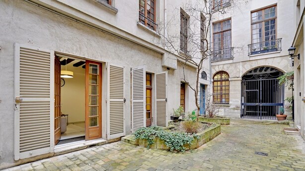 A courtyard with a cobblestone floor, a wooden bench, and a small garden area with plants. - Charming Marais Historic Studio (Paris)