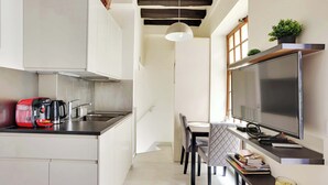 A compact kitchen with a coffee maker, a flat-screen TV, and a dining area with a table and chairs. - Charming Marais Historic Studio (Paris)