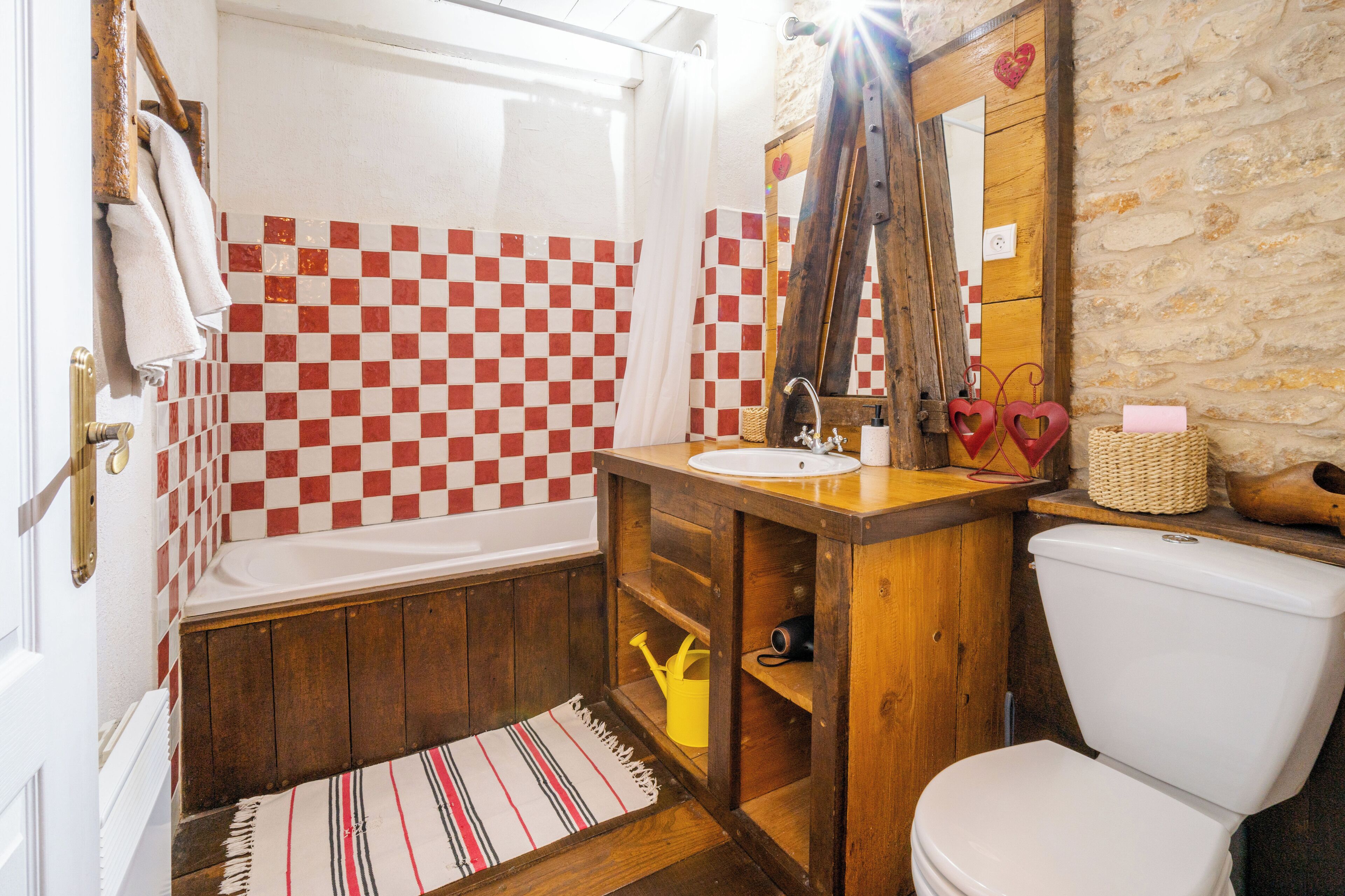A bathroom with a checkered tile wall, a wooden vanity, a white sink, a toilet, and a shower curtain.