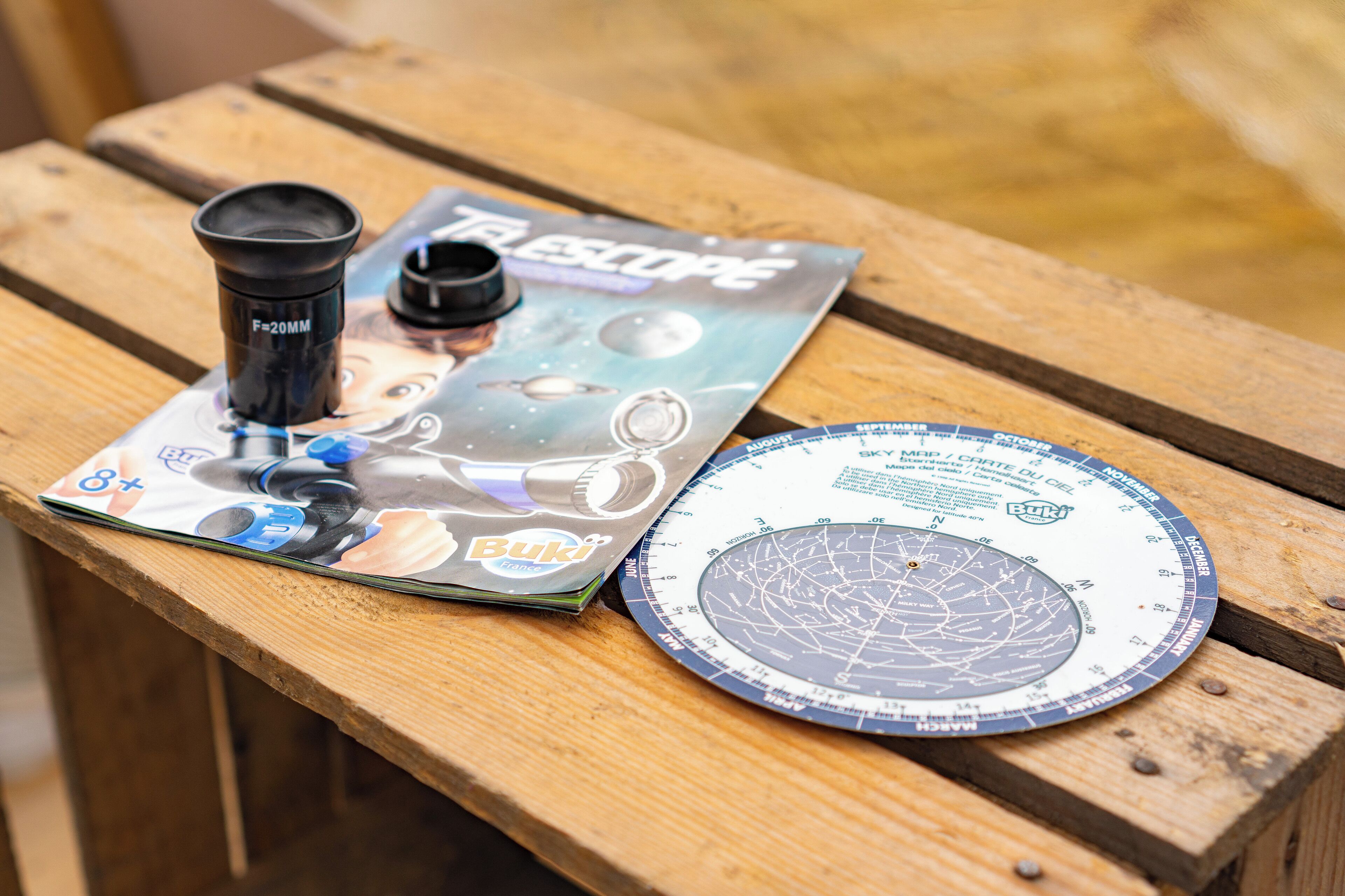 A telescope, a star chart, and a booklet on a wooden table.