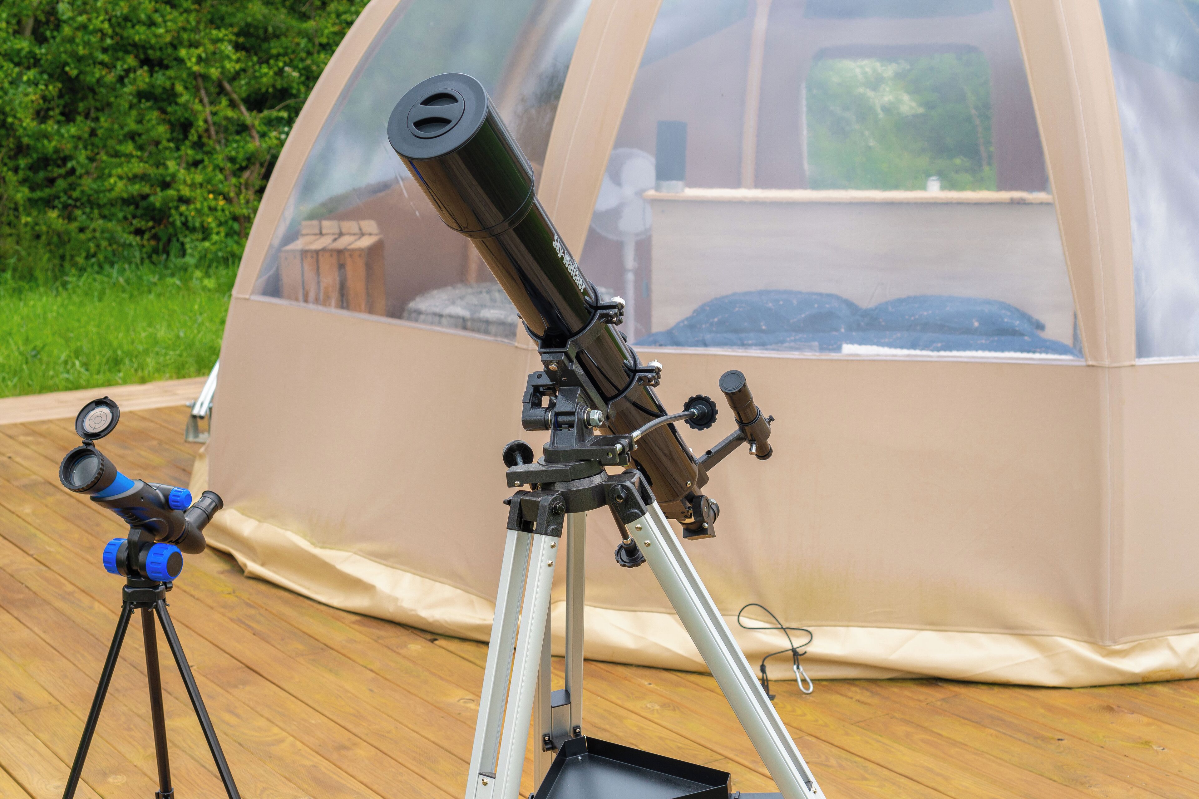 Un telescopio sobre un trípode instalado en una terraza de madera, con una tienda de campaña en forma de cúpula al fondo.