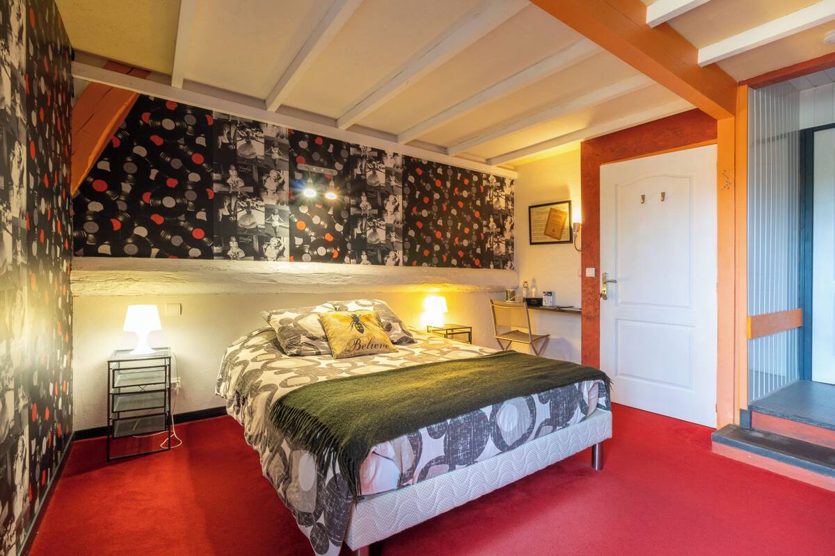Un dormitorio con una cama, dos lámparas de noche, una pared con estampado de lunares, una puerta y una ventana.