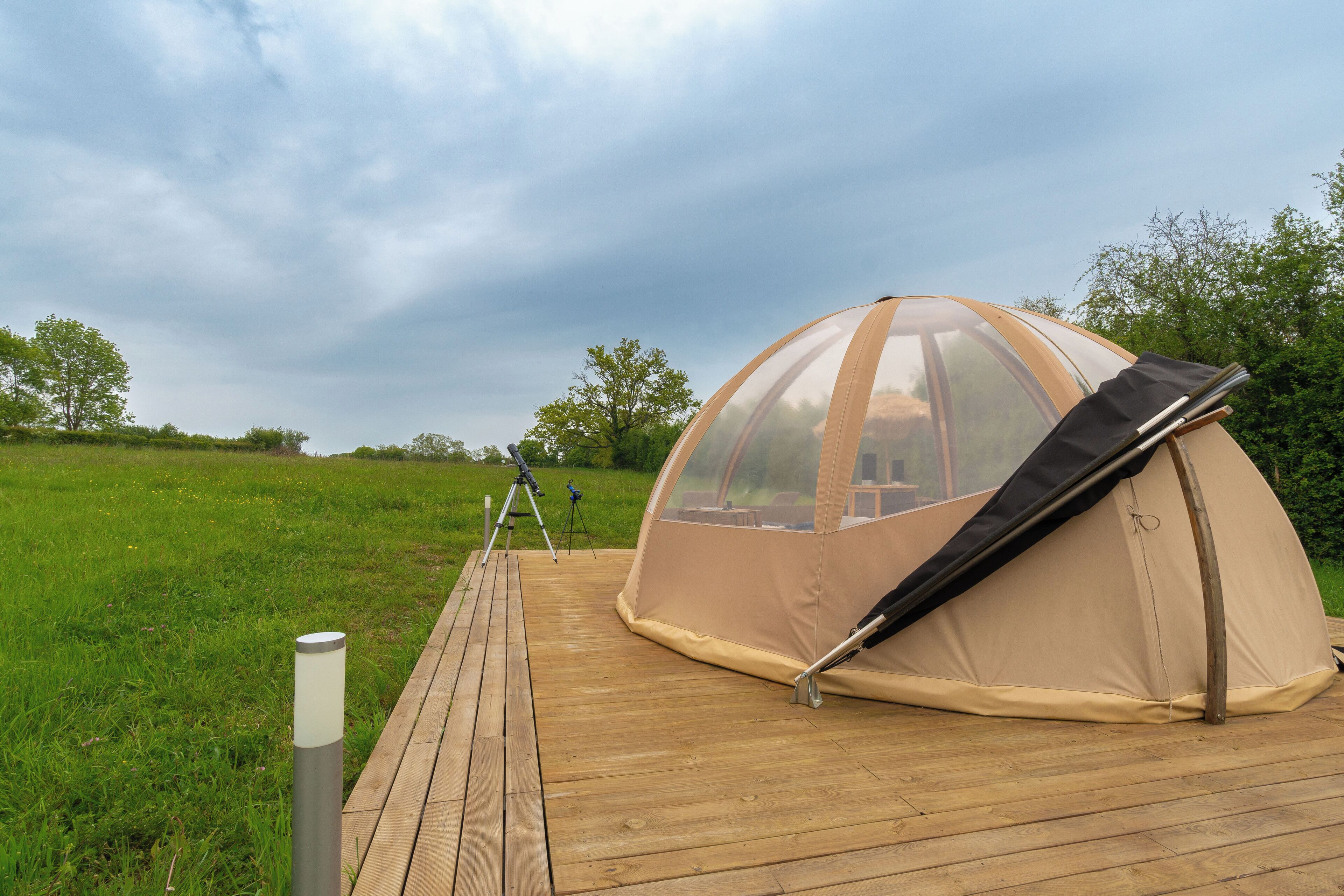 Una tienda tipo cúpula sobre una terraza de madera con un campo de césped al fondo.