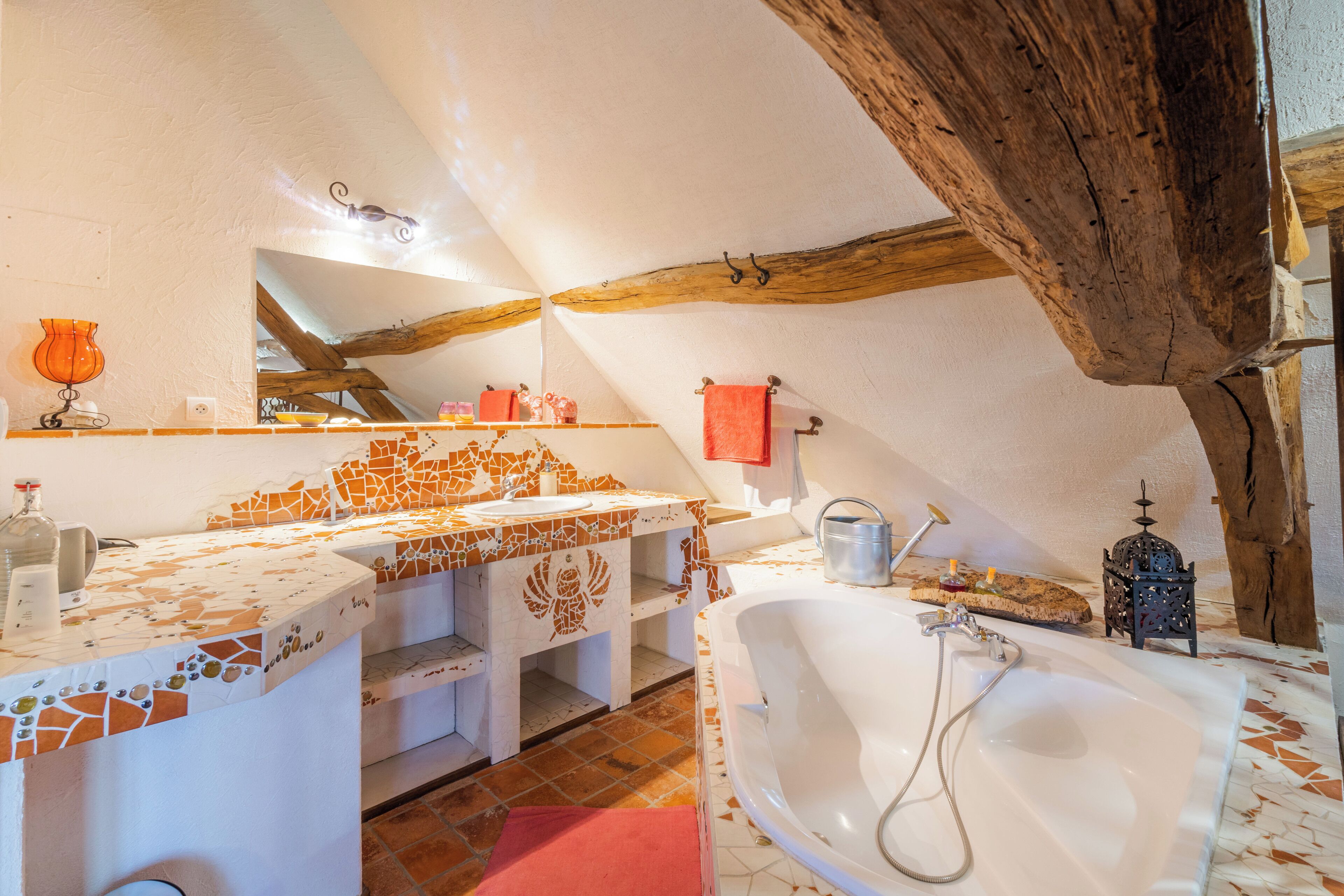 Un baño con una bañera grande, un lavabo con un respaldo de mosaicos y vigas de madera en el techo.