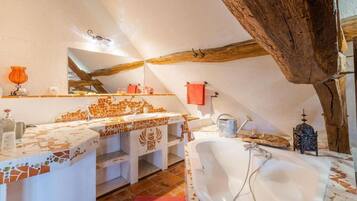 A bathroom with a large bathtub, a sink with mosaic tiles, and a wooden ceiling beam.