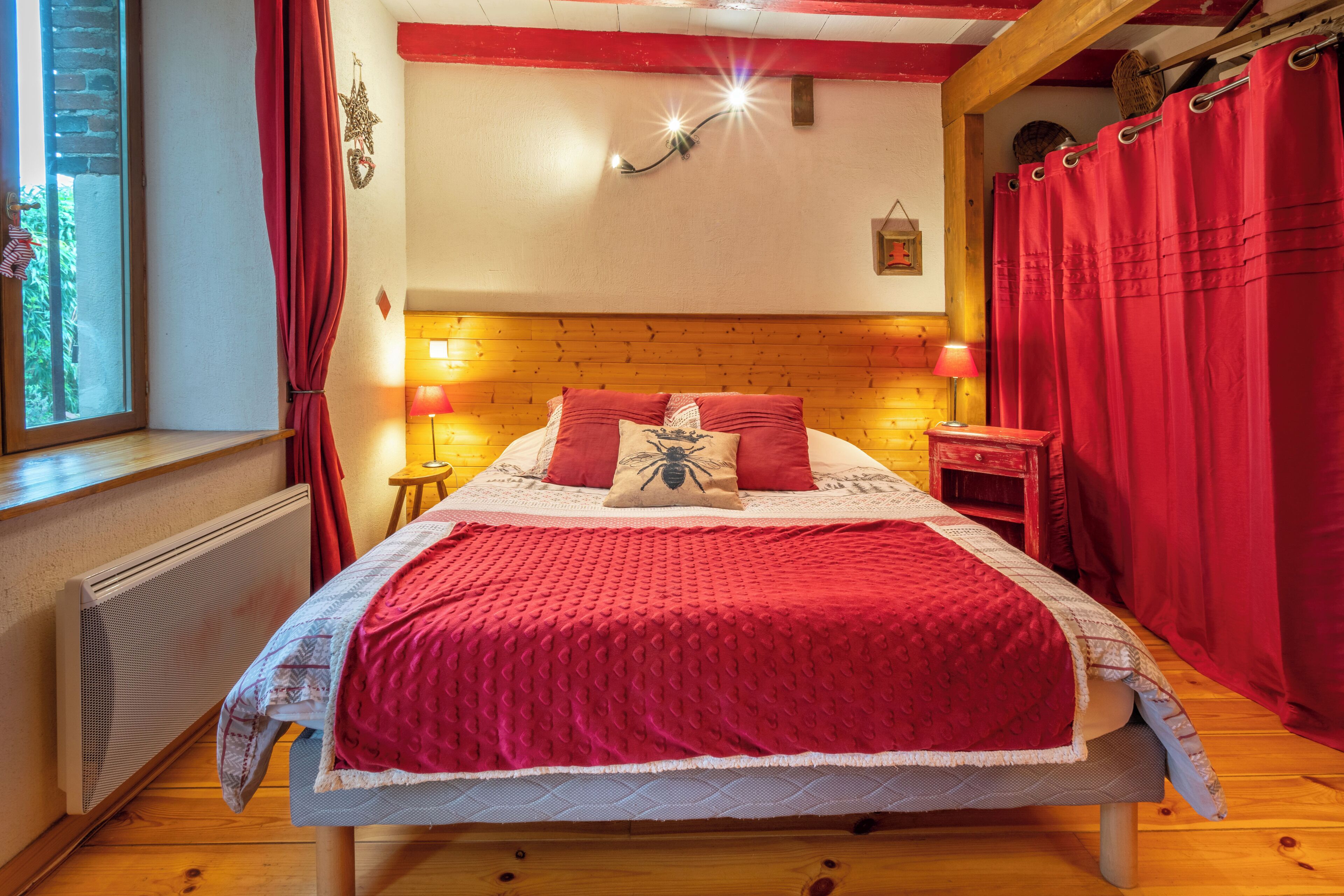 A bedroom with a wooden headboard, a red bedspread, and a window with red curtains.