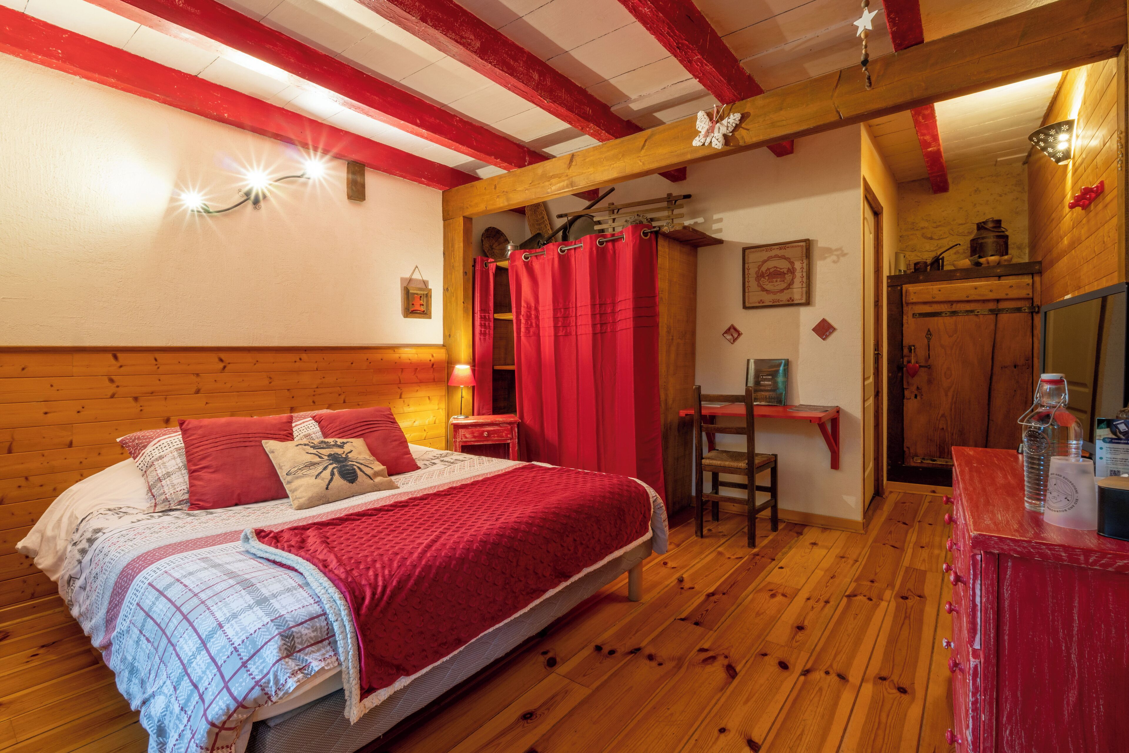 Un dormitorio acogedor con una cama de madera, cortinas rojas y una pequeña zona de escritorio.
