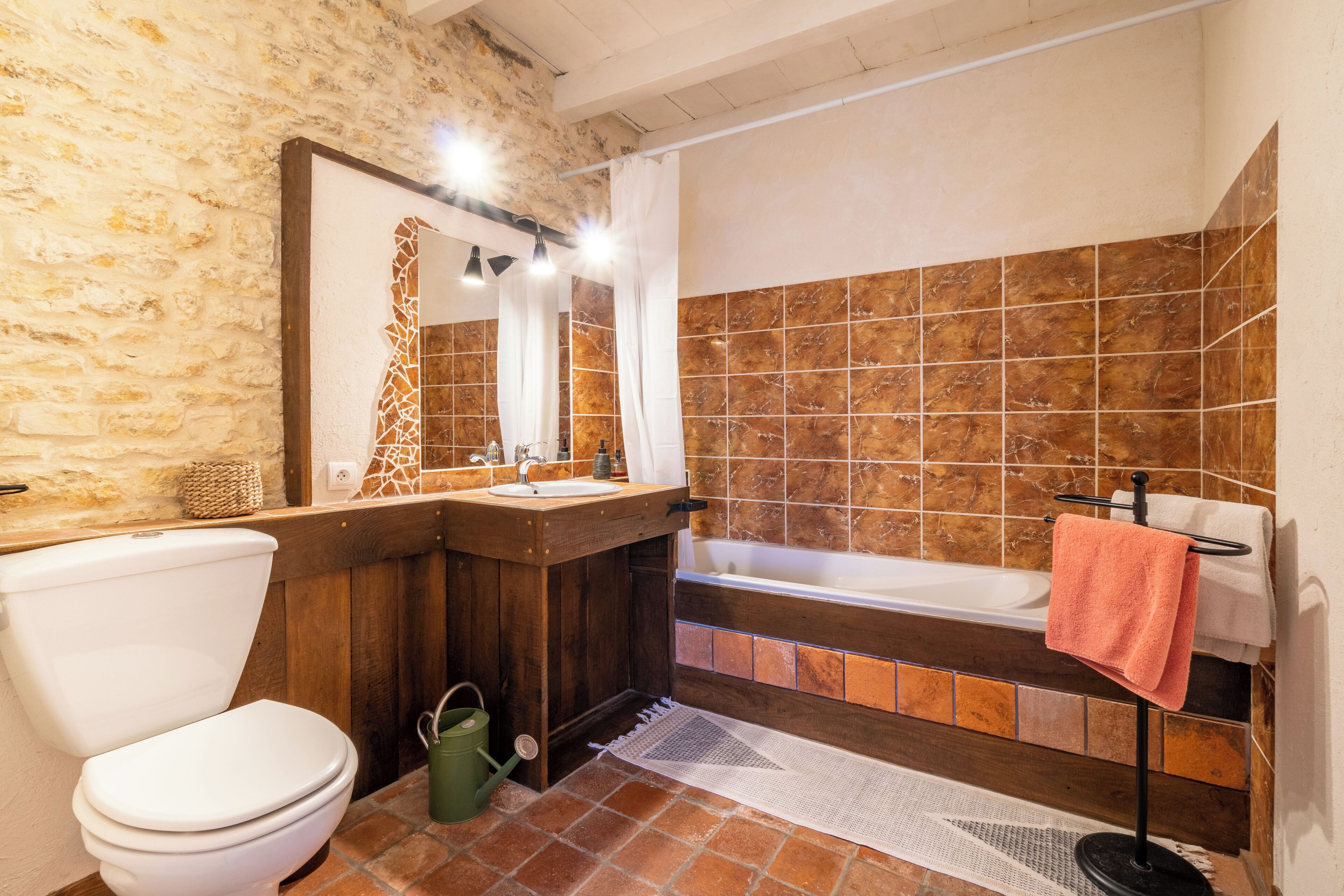 Un baño con pared de piedra, tocador de madera, inodoro blanco y bañera.