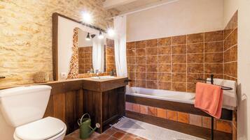 Un baño con pared de piedra, tocador de madera, inodoro blanco y bañera.