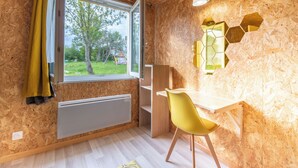 Una habitación con un ventanal grande, un radiador, una silla amarilla y un escritorio de madera.