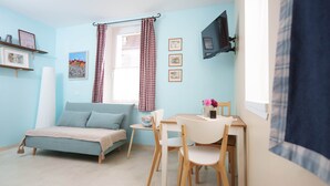 A room with a bed, a desk, and a chair. There are two windows with curtains, a shelf with pictures, and a mounted TV. - Gîte La Schlàppe / 3 persons (HERRLISHEIM PRES COLMAR)