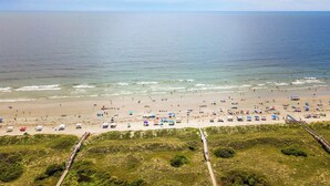 Ein Strand mit einer Holzpromenade, die zum Ufer führt, feinem Sand und Blick aufs Meer.
