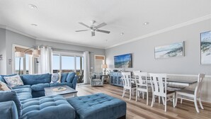 Ein geräumiges Wohnzimmer mit einer Eckcouch, einem Essbereich mit weißen Stühlen und einem Deckenventilator.
