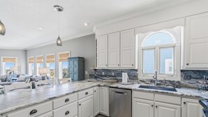 A kitchen with white cabinets, a marble countertop, a dishwasher, and a window with a view. - Renovated Ocean Front Dream House in Sunset Beach (Sunset Beach)