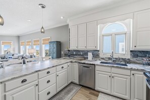 Una cocina con armarios blancos, encimera de mármol, lavavajillas y ventana con vistas.