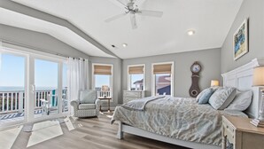 A bedroom with a bed, a chair, a nightstand, a clock, and a view of the outside. - Renovated Ocean Front Dream House in Sunset Beach (Sunset Beach)