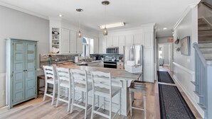 A spacious kitchen with white cabinetry, a wooden island, and a dining area with white chairs. - Renovated Ocean Front Dream House in Sunset Beach (Sunset Beach)