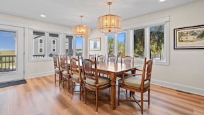 Une salle à manger avec une grande table en bois, plusieurs chaises et deux luminaires suspendus.