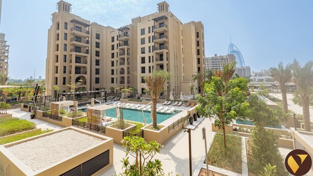 A high-rise building with a rooftop pool area, surrounded by greenery and palm trees. - Vogue | Jadeel Madinat Jumeirah near Burj Al Arab (Dubai)