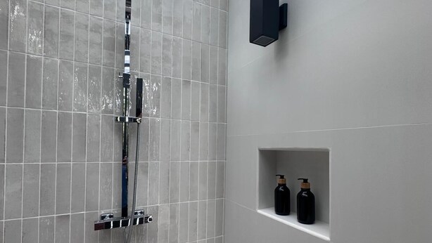 A modern shower with a rain showerhead, a handheld showerhead, and a wall-mounted control panel. There is a small shelf with two bottles of shampoo and conditioner. - Palmera Azul (Bejuco)