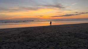 Een strand bij zonsondergang, met iemand die langs de kust wandelt.