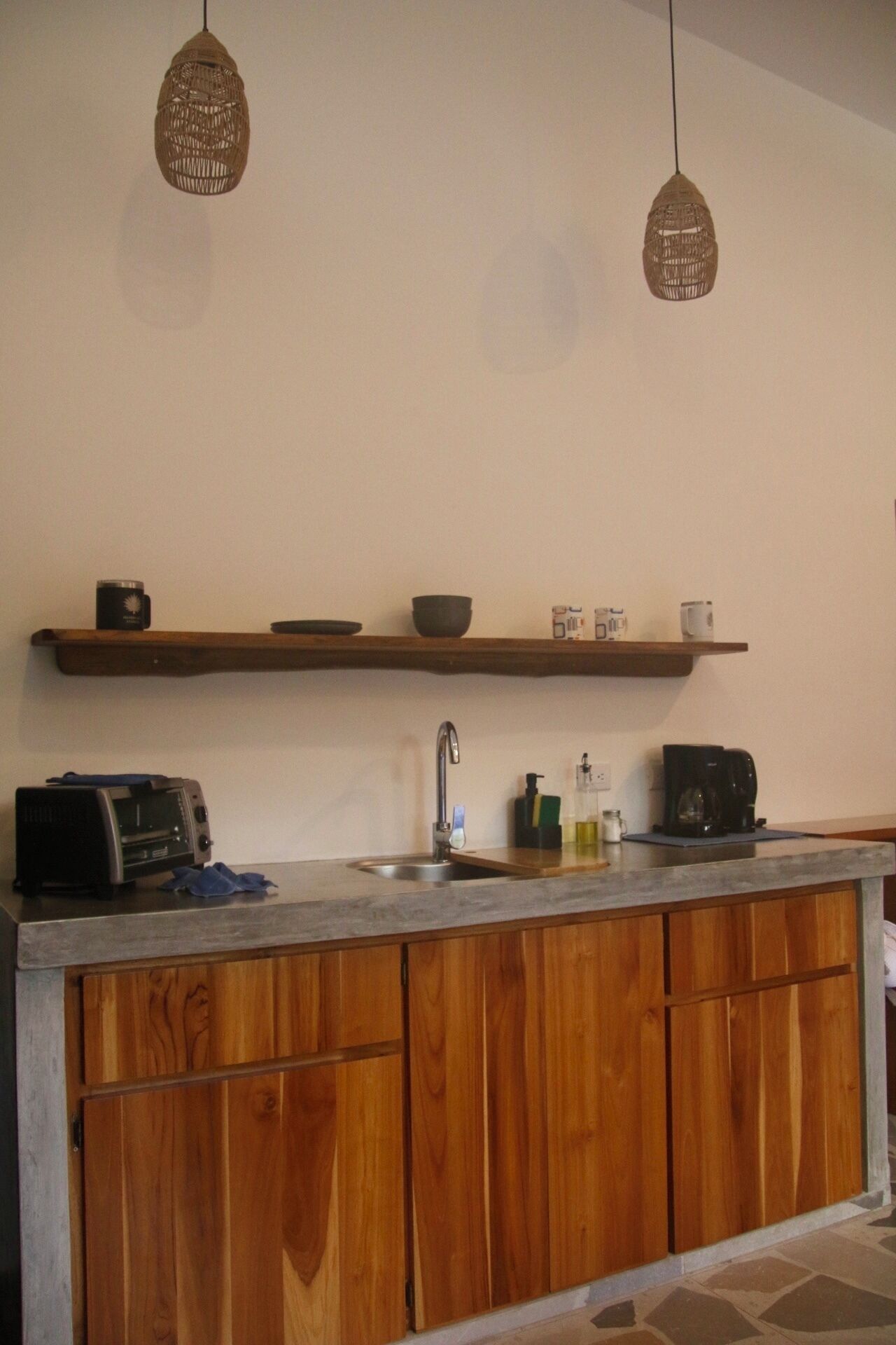 A kitchen with wooden cabinets, a built-in sink, a toaster, and hanging wicker pendant lights.