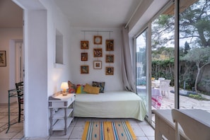 A bedroom with a bed, a desk, a chair, a lamp, and a window with a view of the outdoors.