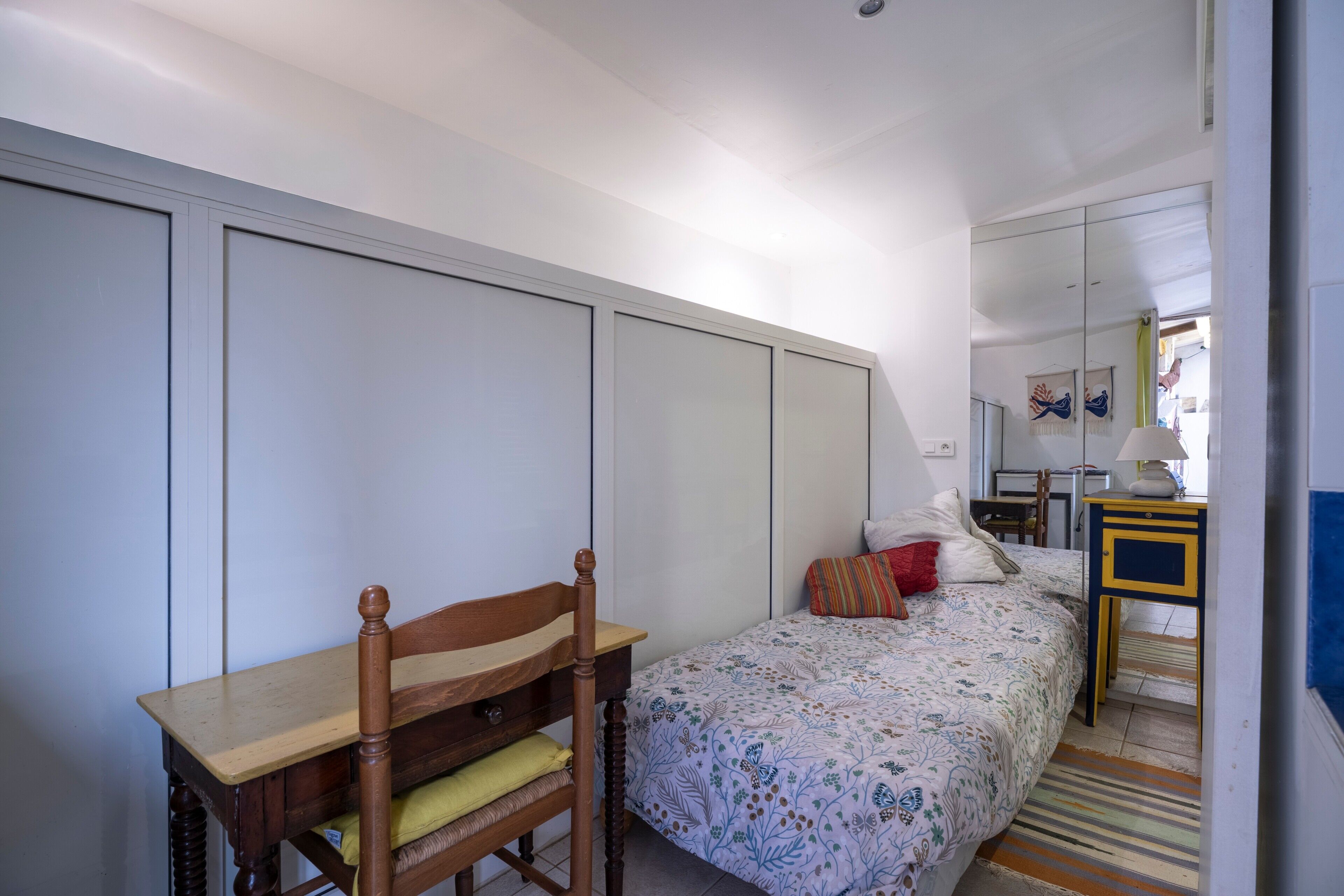Een slaapkamer met een bed, een houten stoel, een bureau en een spiegel.