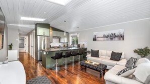 A modern kitchen with a central island, bar stools, and a dining area with a sofa and coffee table. - Knockan Hill Rentals - Garden Suite (Victoria)