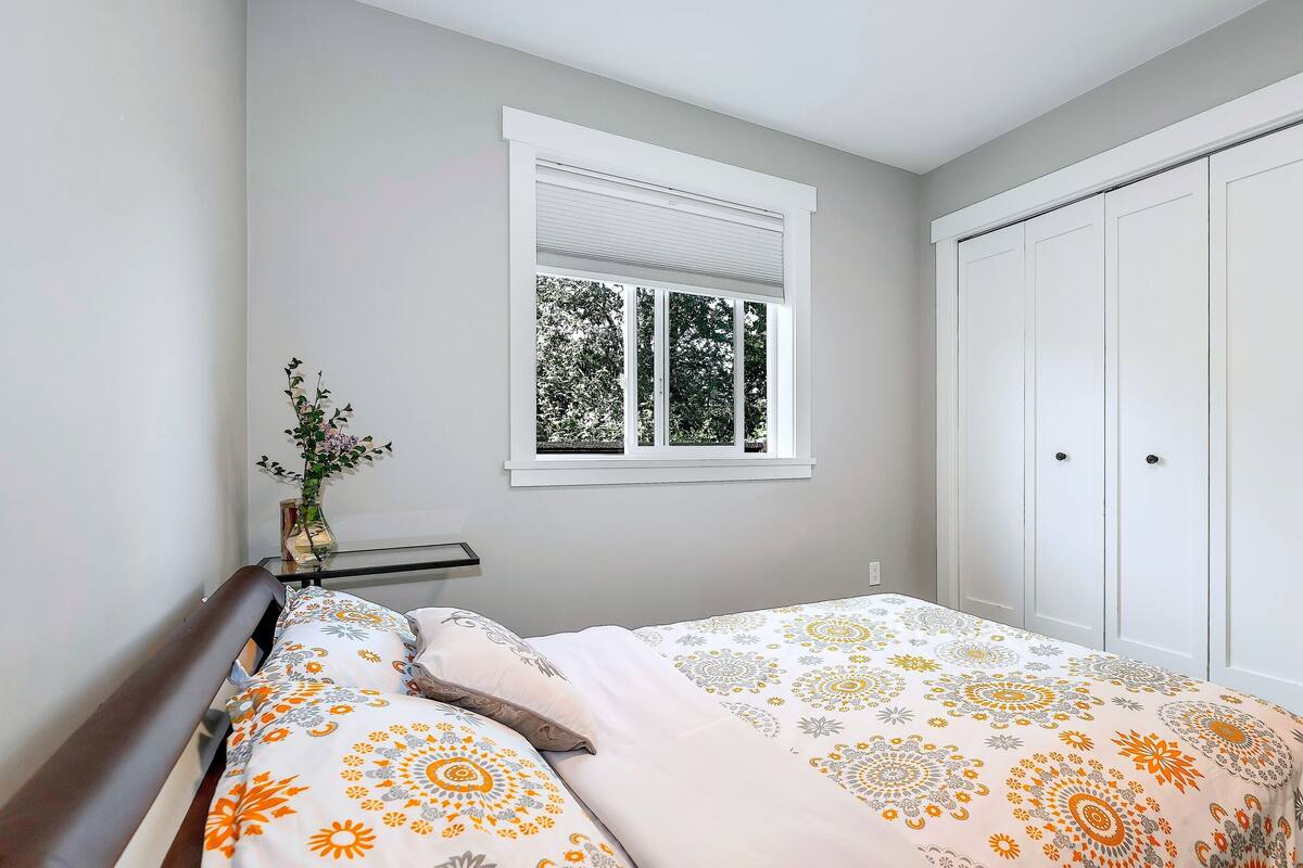 Un dormitorio con cama, una ventana con persianas, un armario blanco y una mesita con un jarrón.
