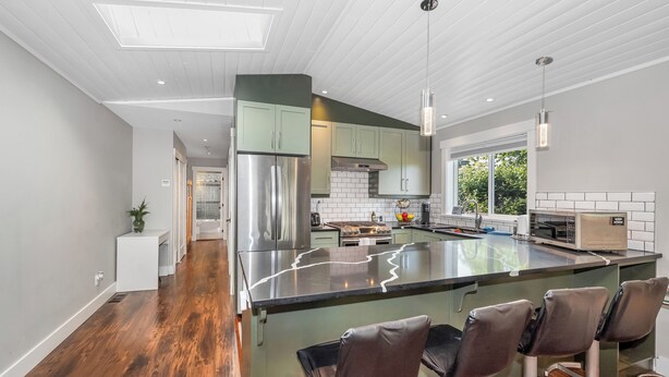 A modern kitchen with a central island, stainless steel appliances, and a view to the outdoors. - Knockan Hill Rentals - Garden Suite (Victoria)