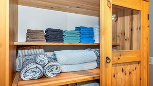 A wooden cabinet with shelves holding folded towels in various colors. - Knockan Hill Rentals - Garden Suite (Victoria)