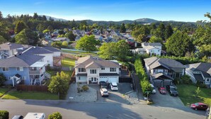 A residential area with houses, a clear sky, and a hilly landscape in the background. - Knockan Hill Rentals - Garden Suite (Victoria)