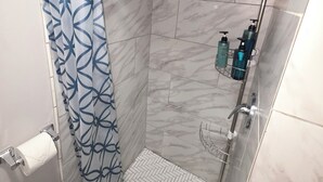 A shower with a patterned curtain, a handheld showerhead, and toiletries on a shelf. - Bluff City Studio: B (Millington)