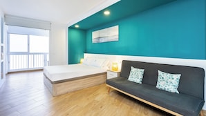 A bedroom with a bed, a sofa, a nightstand, and a window. - Atlantic View Studio in Mesa del Mar (Mesa del Mar)