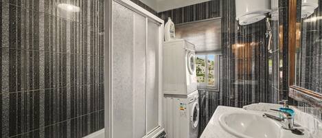 A bathroom with a large mirror, a sink, a washing machine, and a shower.
