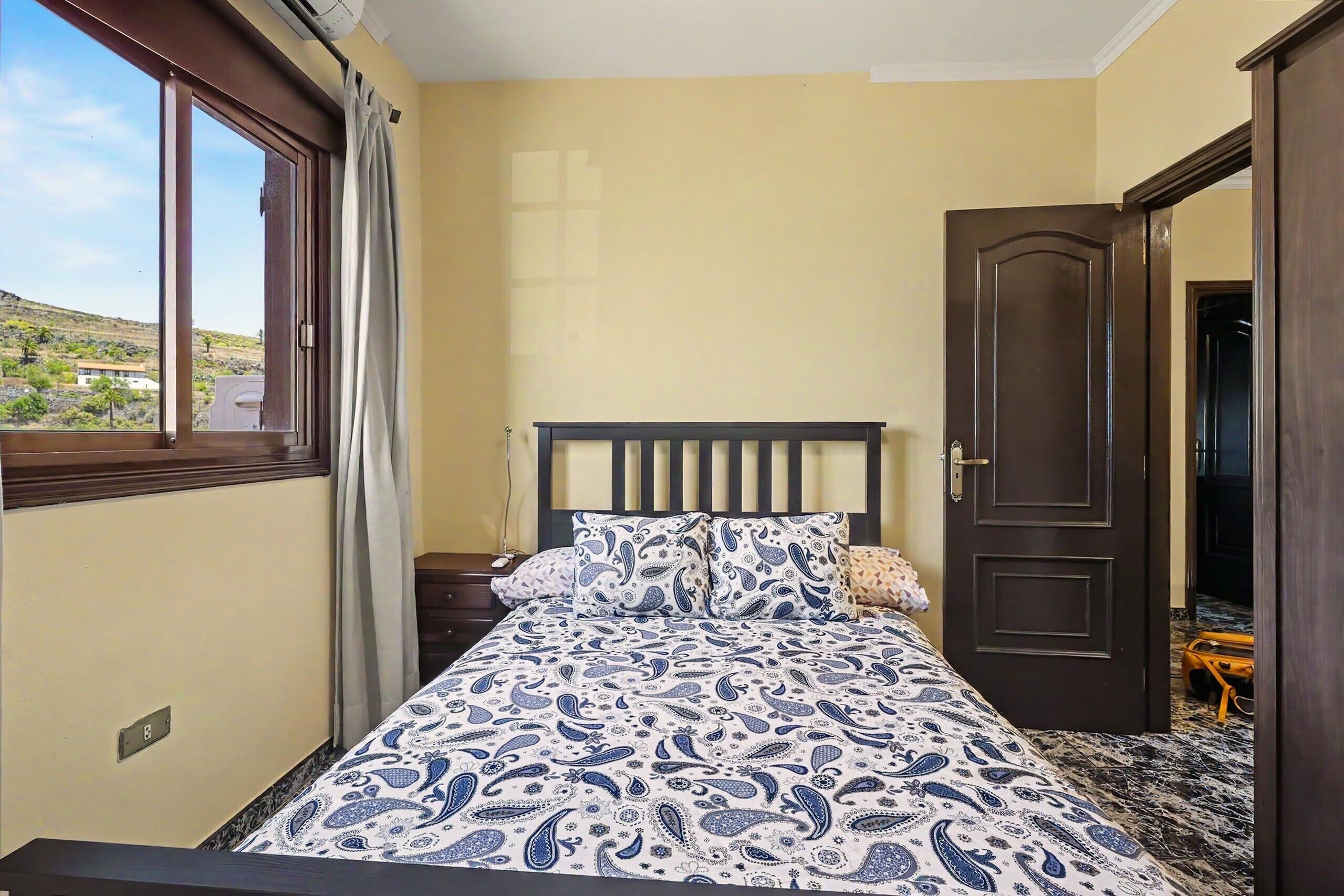 Un dormitorio con cama, ventana, puerta y vistas al exterior.