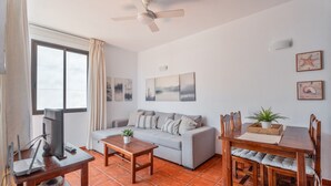 A living room with a sofa, a wooden table, a TV, and a ceiling fan. - Casa Perla – Terrace & Pool in the Heart of Playa de Santiago (Playa de Santiago)