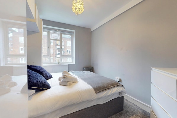 Un dormitorio con cama, ventana, cómoda y lámpara en el techo.