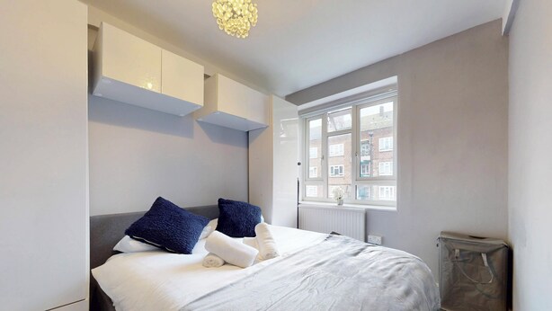 A bedroom with a bed, pillows, a radiator, a window, and a suitcase. - Bright 1Bedroom Home-Brixton Tube 12min Away (Brixton)